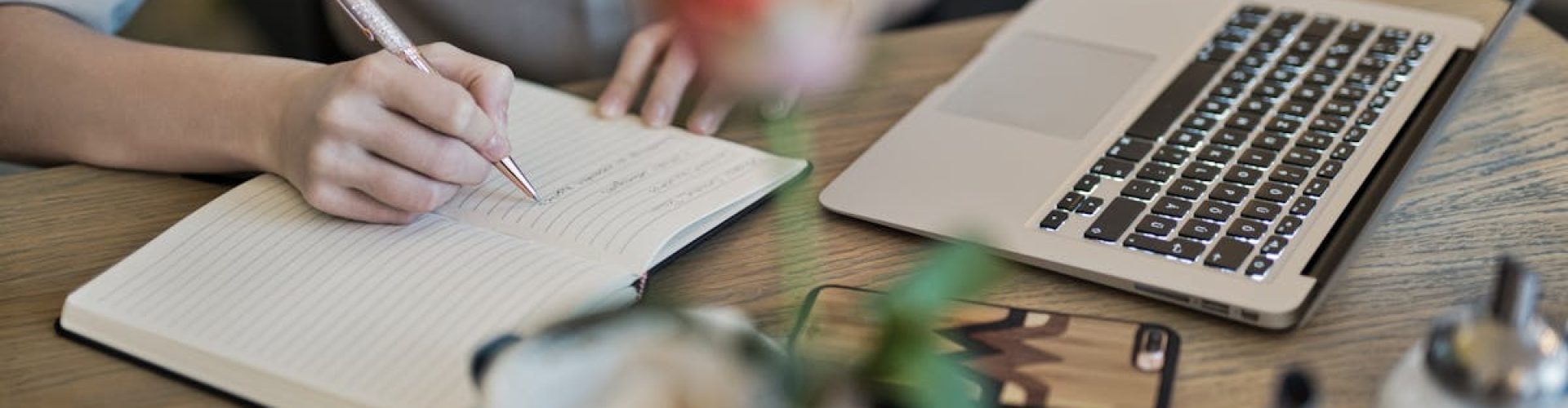 Woman writing in a notebook with a laptop and coffee cup on a desk. Ideal for workspace inspiration.